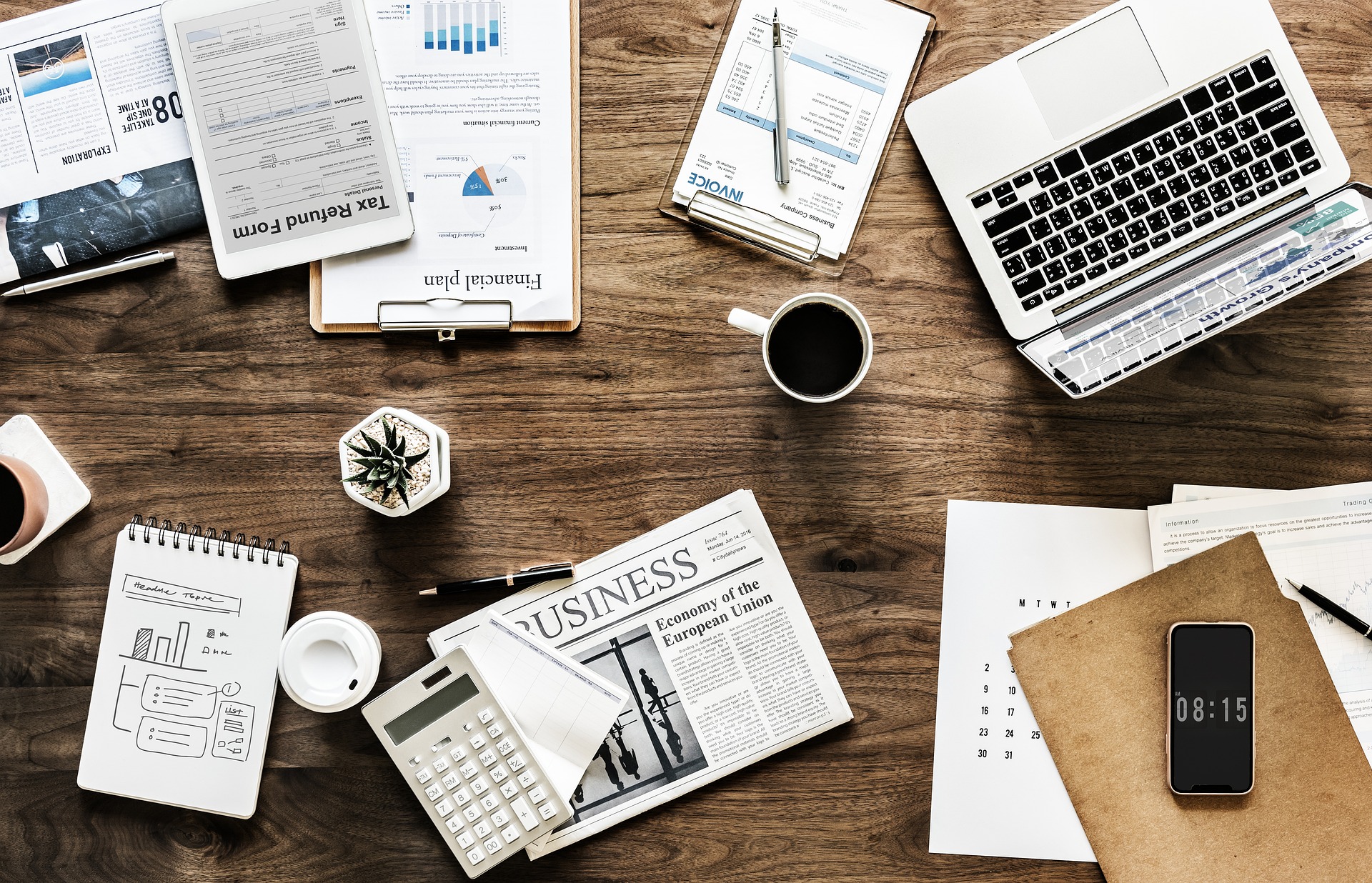 A desk of tax forms, invoices and a laptop